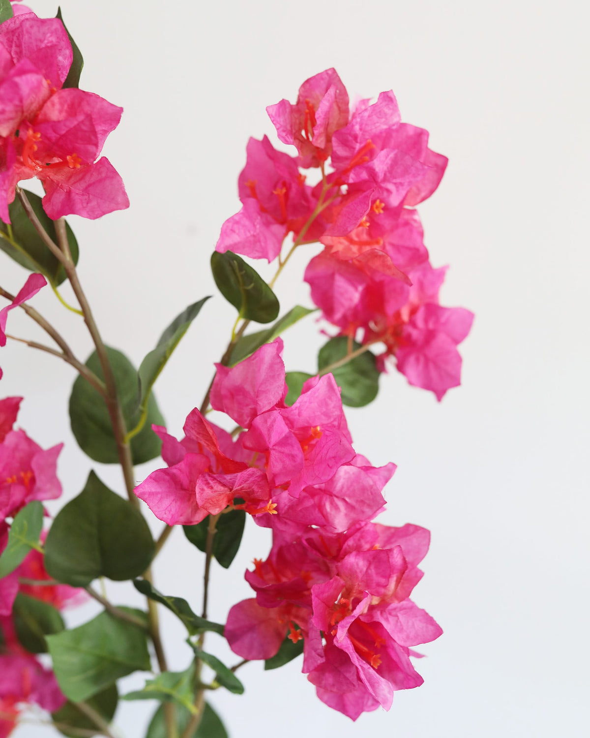 A close-up of a faux bougainvillea branch with bright pink flowers and green leaves against a plain white background.