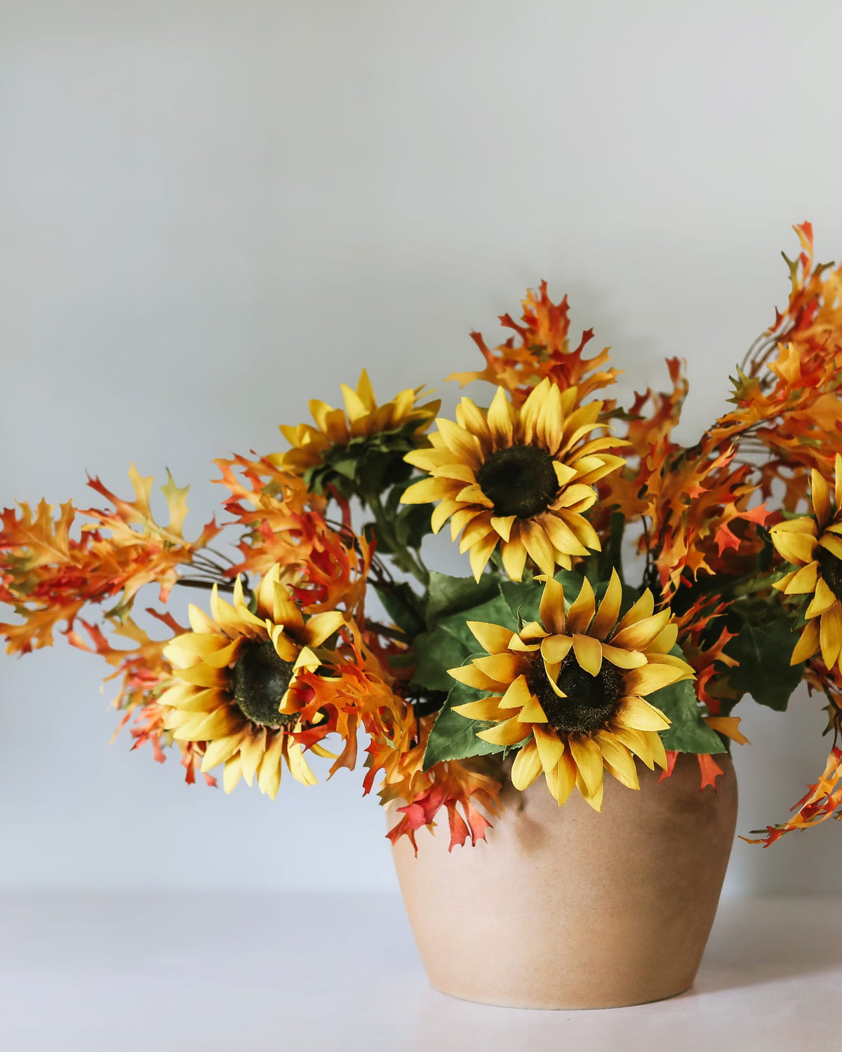 Artificial sunflowers and oak leaves in a vase