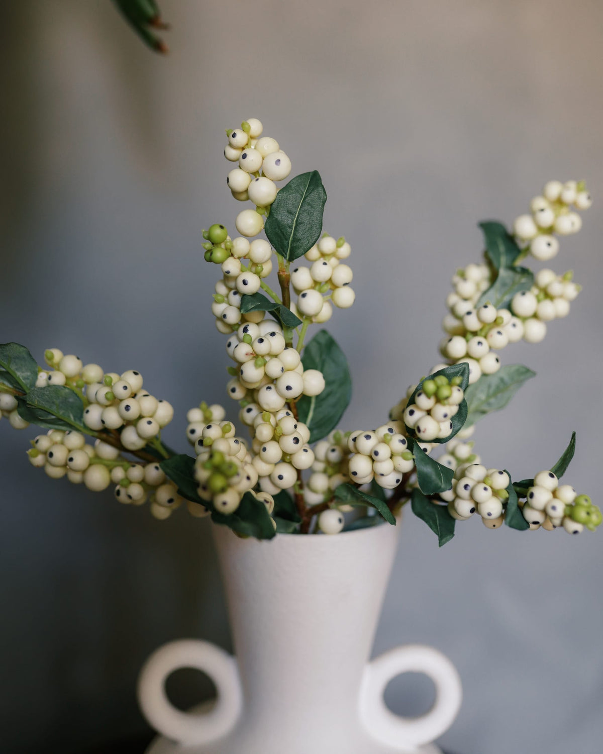 Artificial snow berries in a white vase against a neutral background