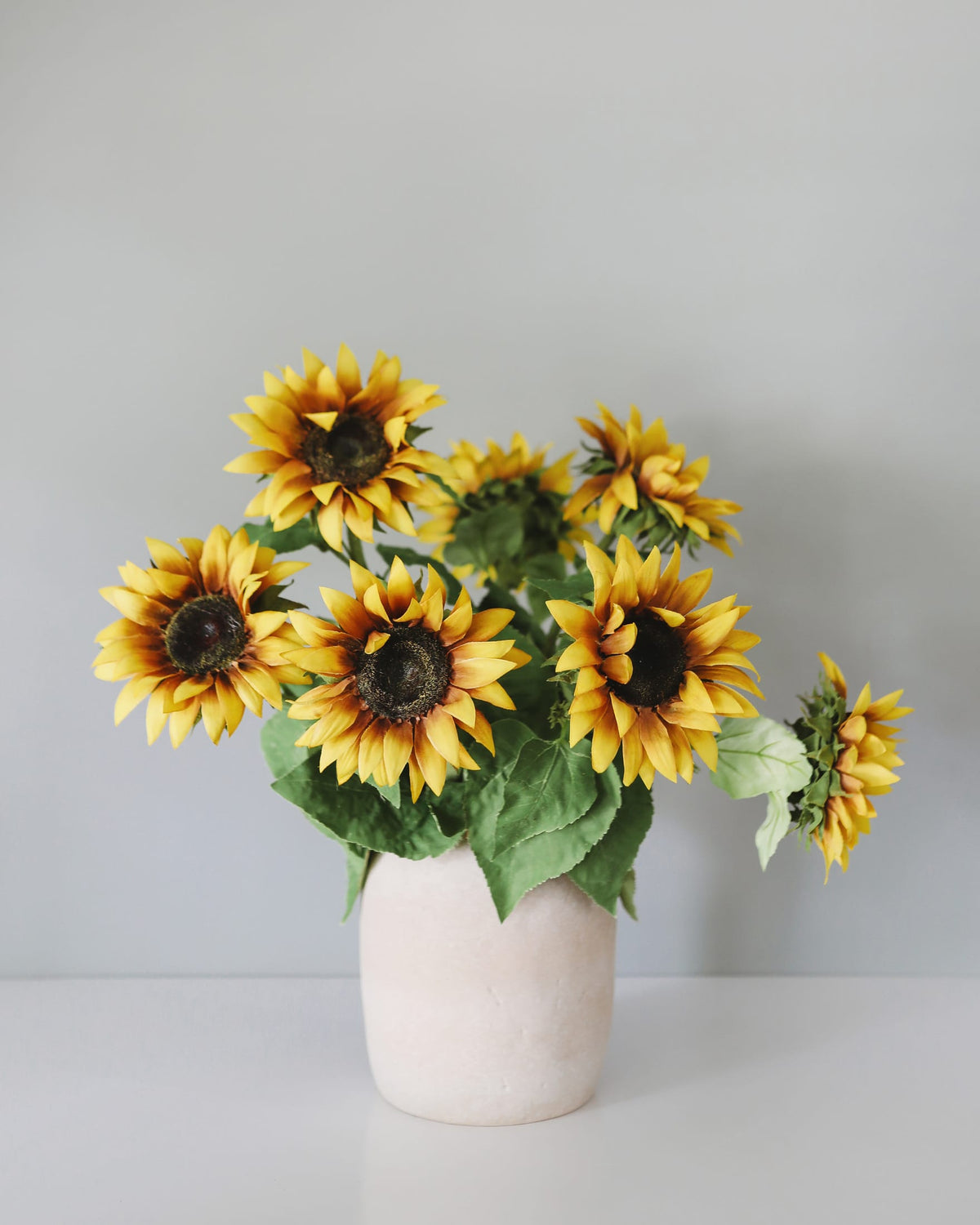 Vase with faux sunflowers on a light gray background