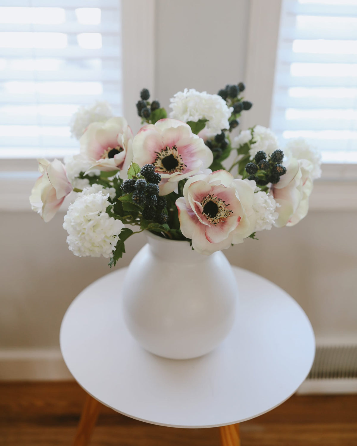 White vase with faux pink and white flowers on a white surface
