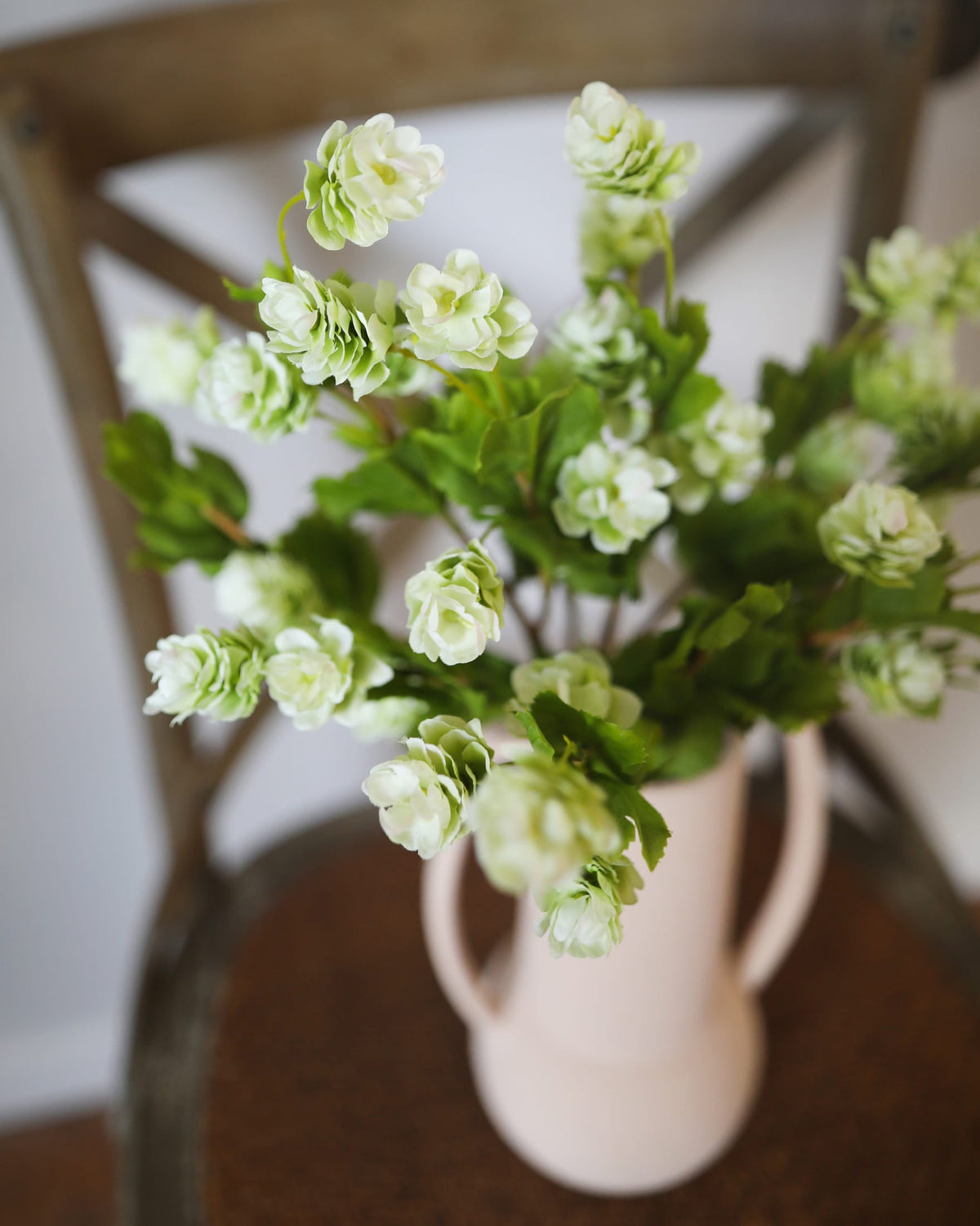 Green artificial hops in a white vase on a wooden chair