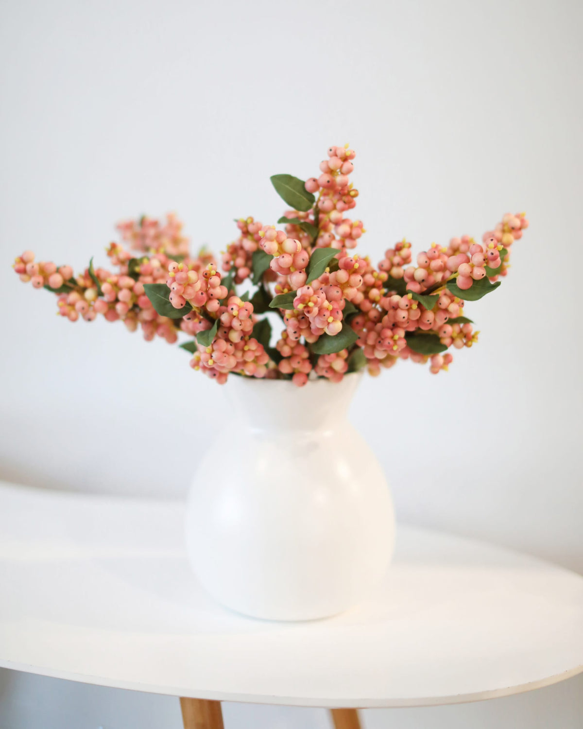 White vase with pink berries on a white surface