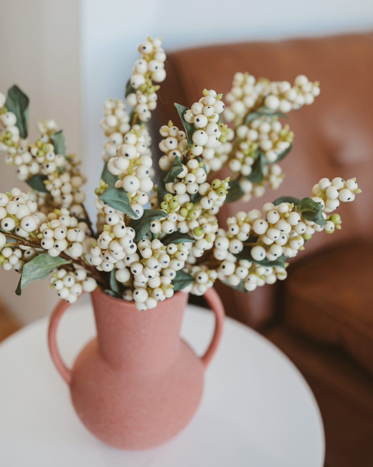 Pink vase with faux snow berry arrangement on a white surface