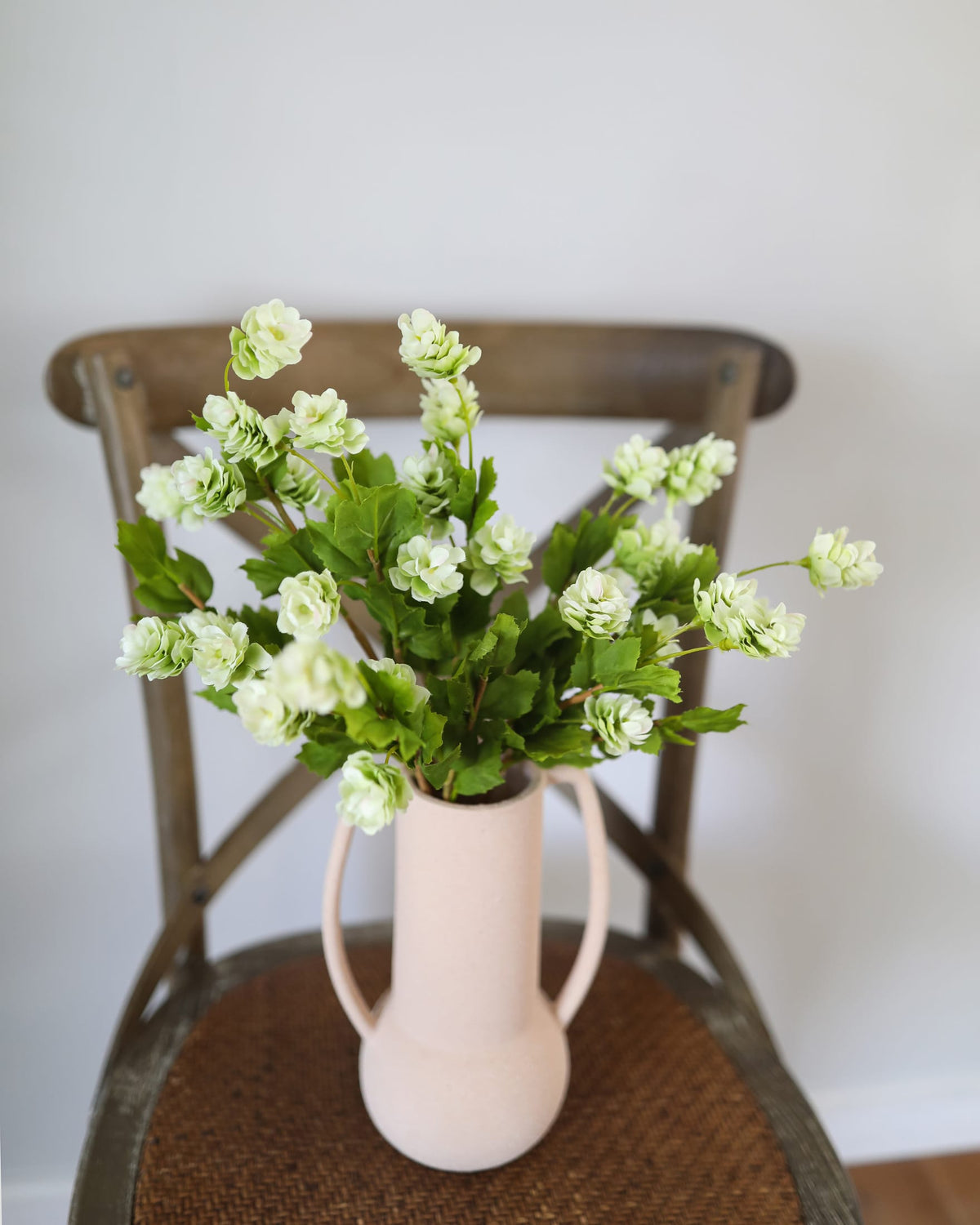 Vase with faux hops on a wooden chair against a white wall