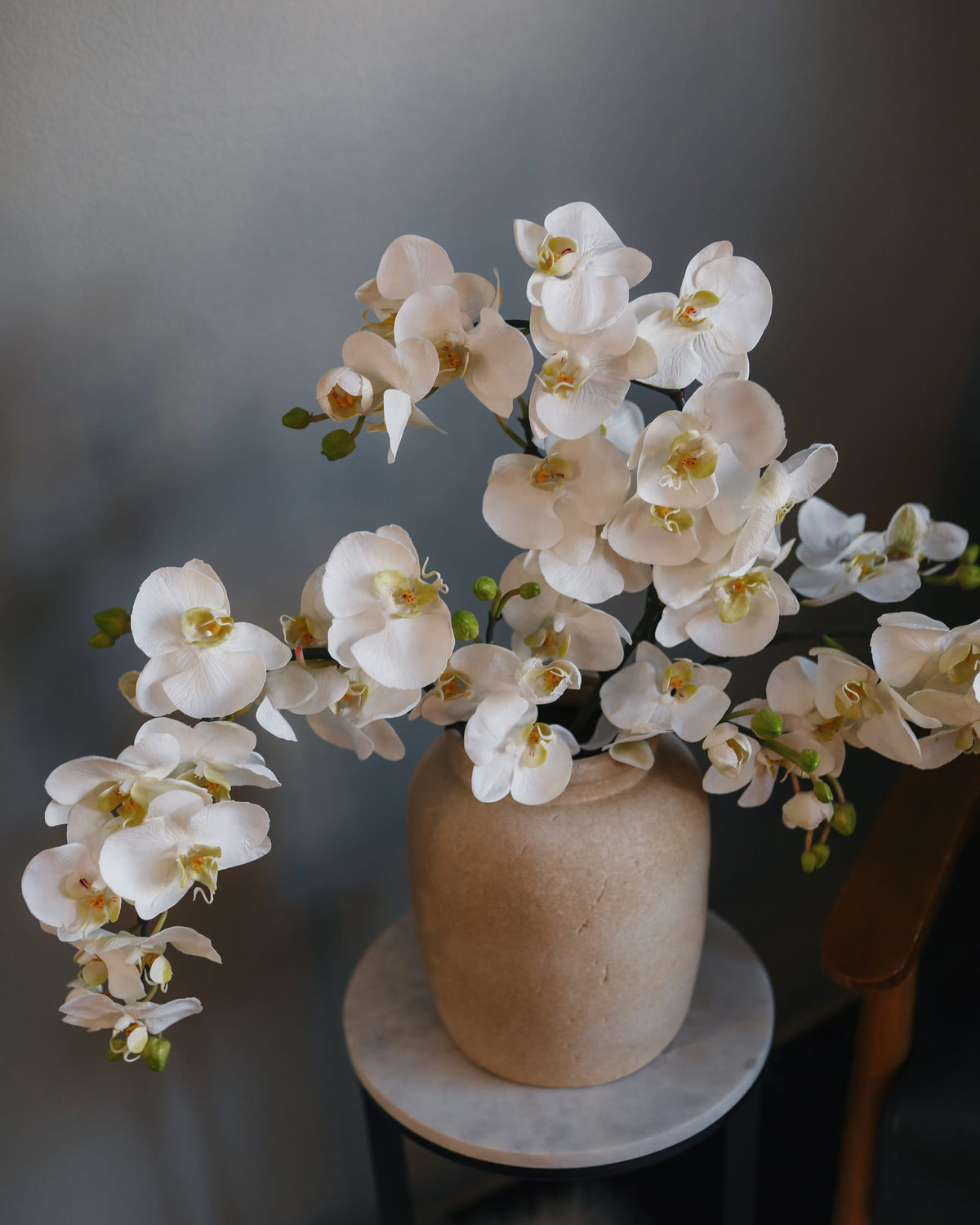 Cascading white artificial Phalaenopsis orchids arranged in a bronze ceramic vase.