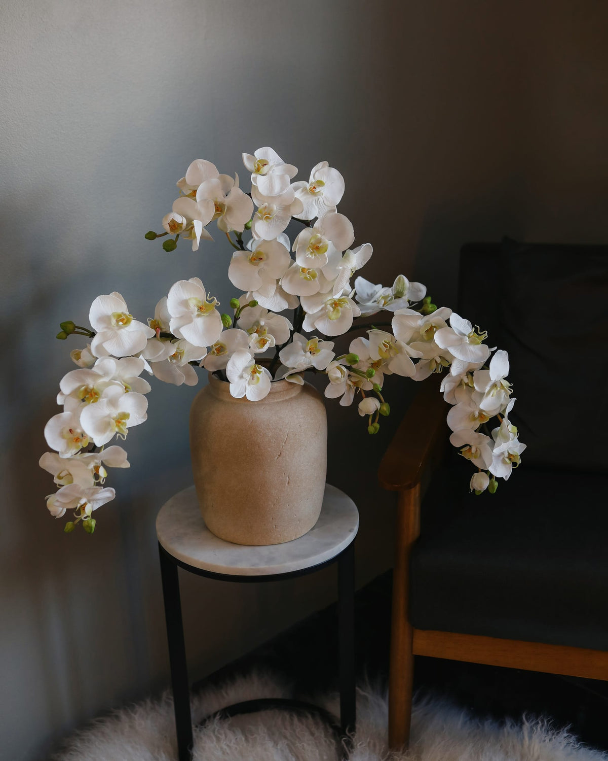 White artificial Phalaenopsis orchids arranged in a ceramic vase in a styled interior.