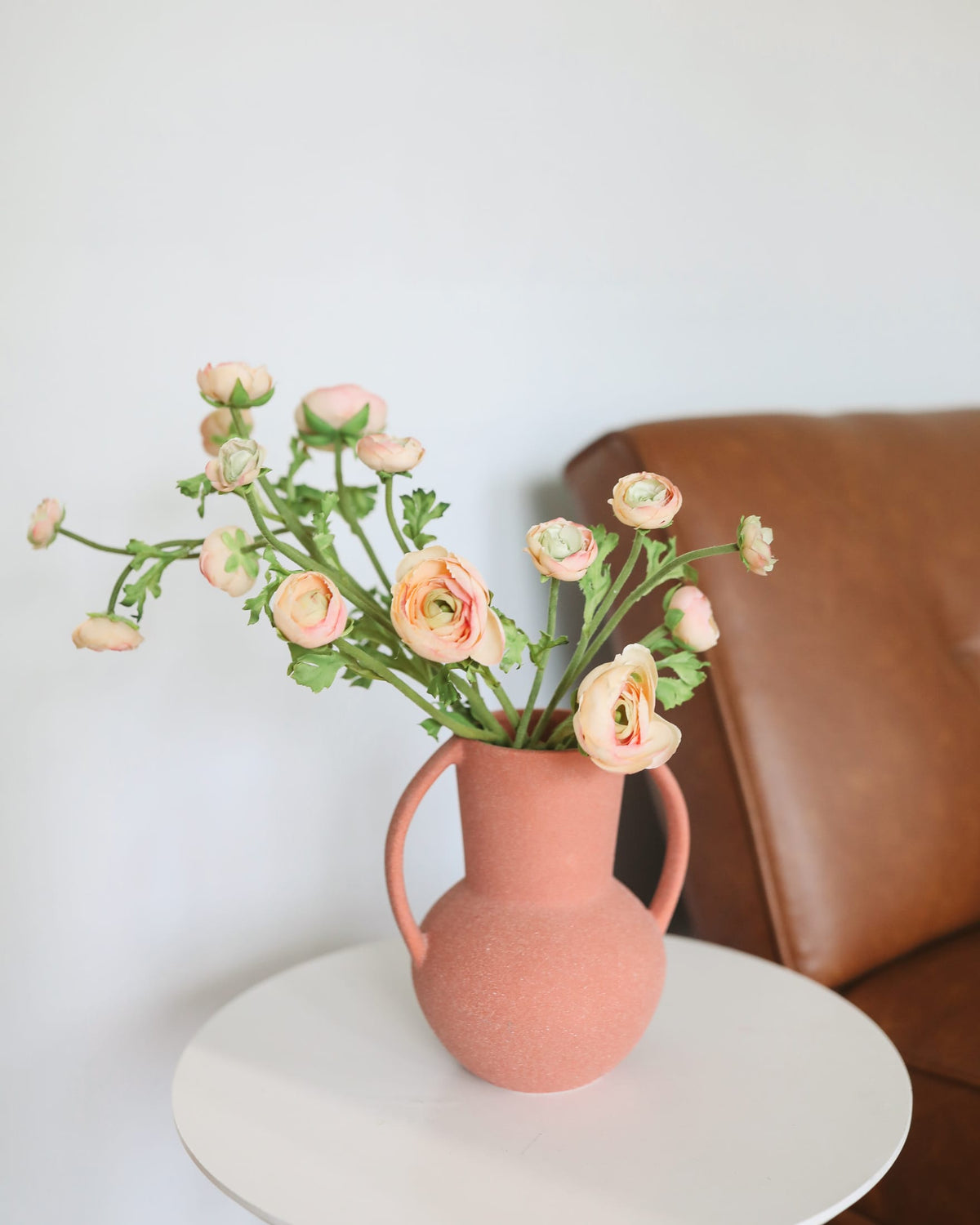 Pink vase with faux ranunculus on a white surface against a neutral background