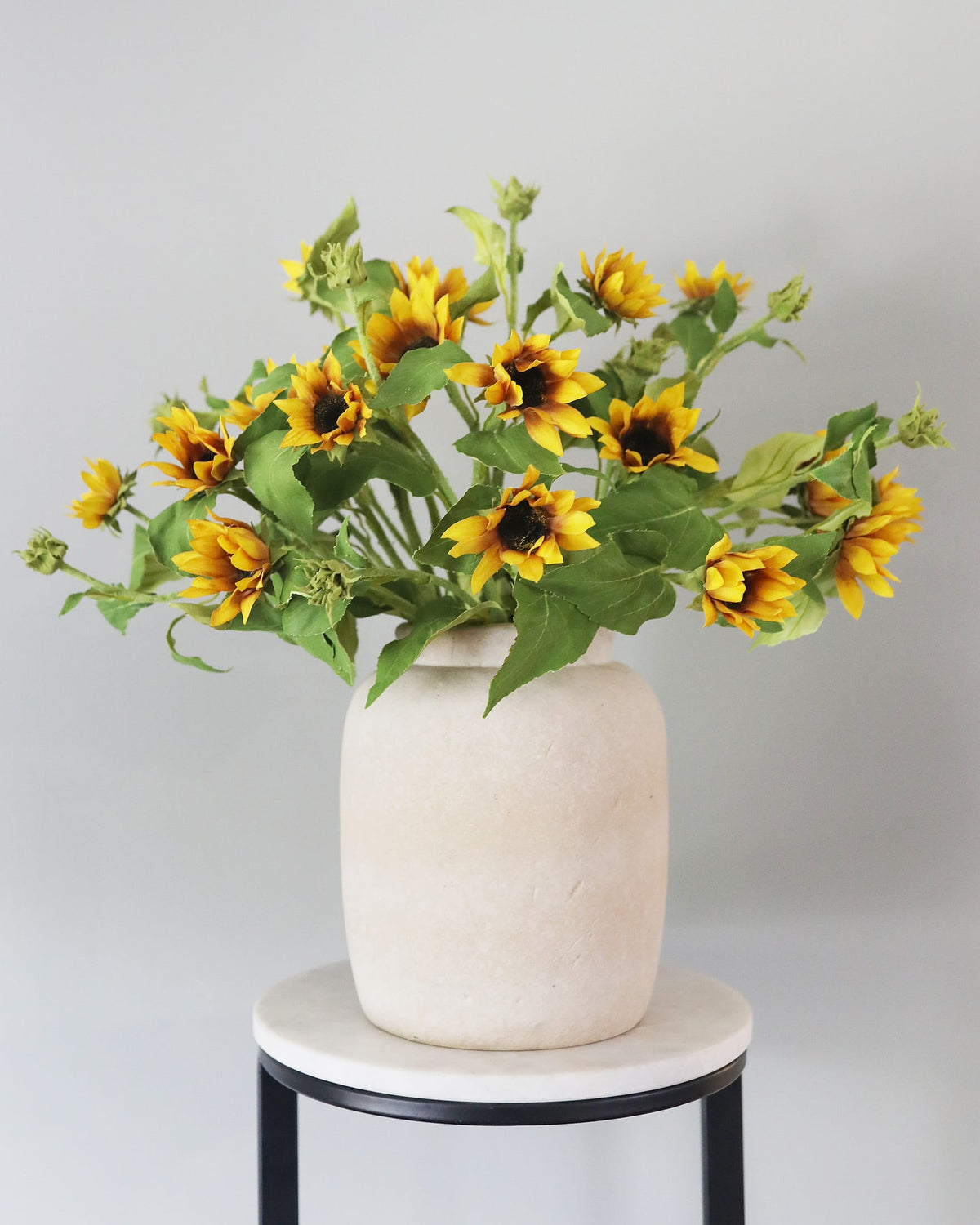 Vase with faux  sunflowers on a small round table against a light gray background
