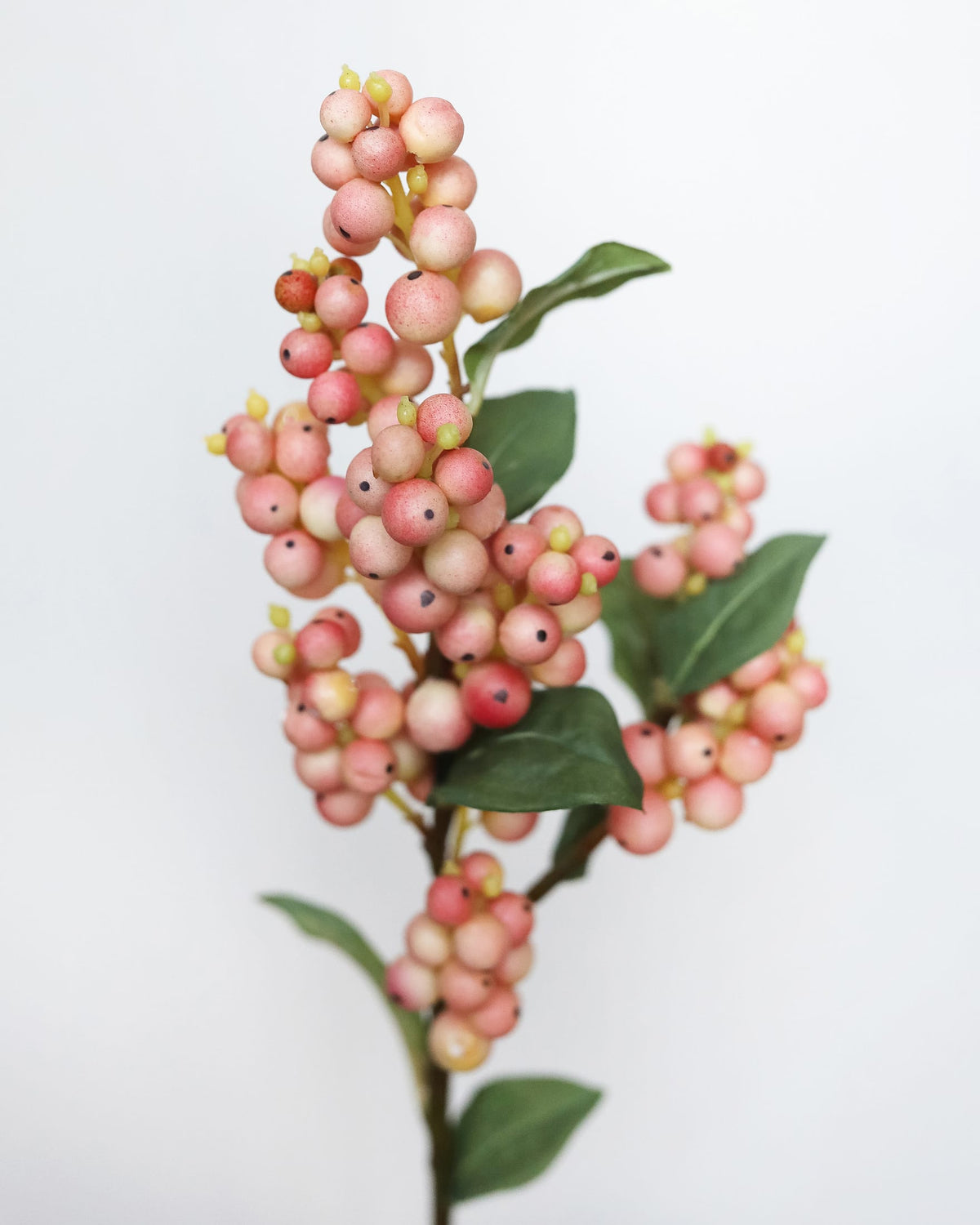 An artificial floral branch featuring clusters of faux pink and cream berries with green leaves, set against a plain white background.