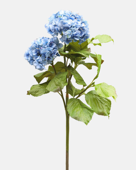 Artificial blue hydrangea flower branch with green leaves on a light gray background