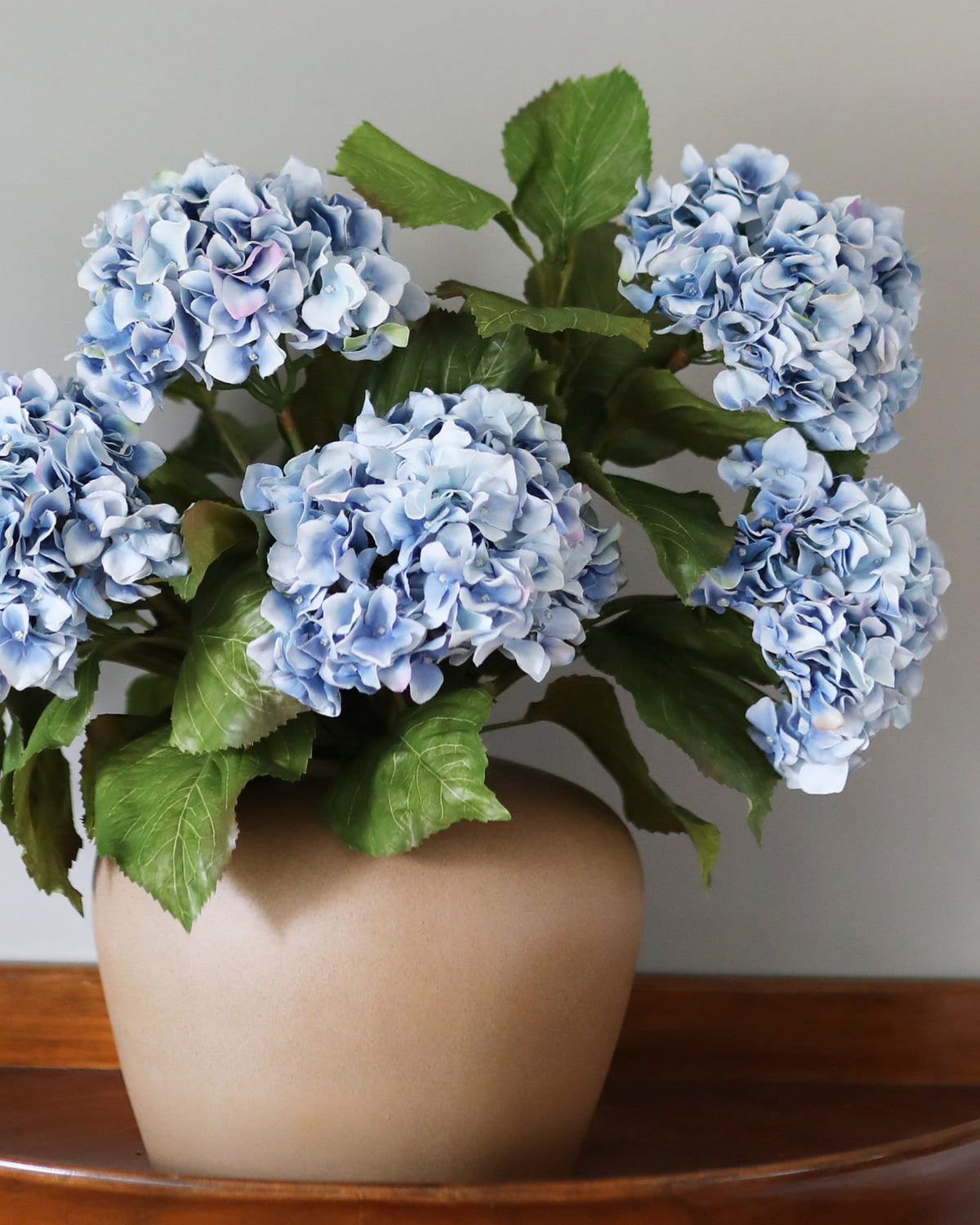 Vase with faux blue hydrangeas on a wooden surface
