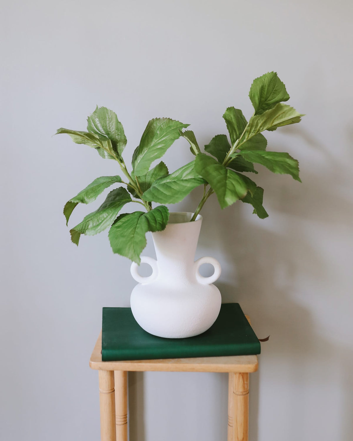 White vase with faux hydrangea leaves on a green surface against a light gray wall