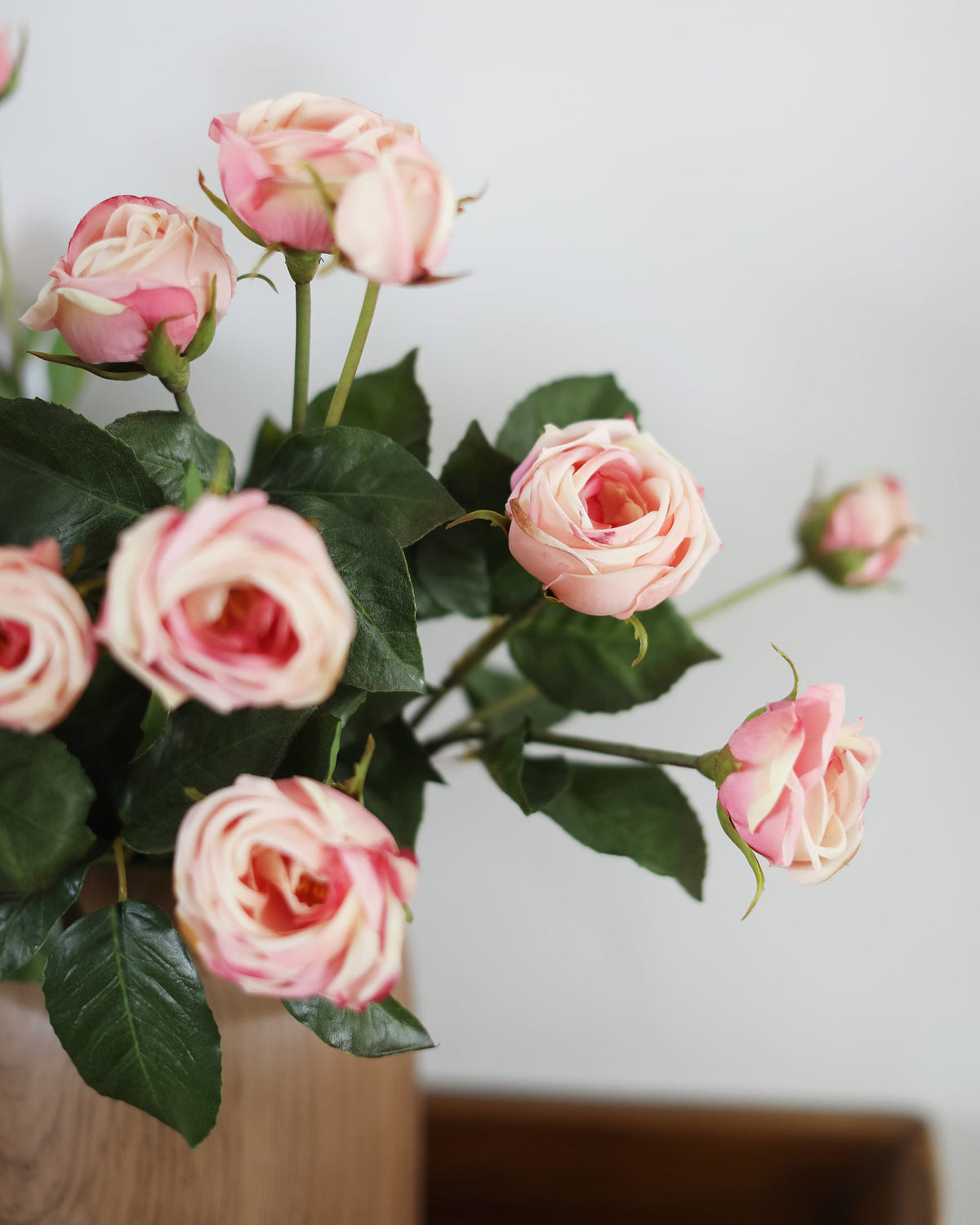 Bouquet of pink artificial roses with green leaves on a light background