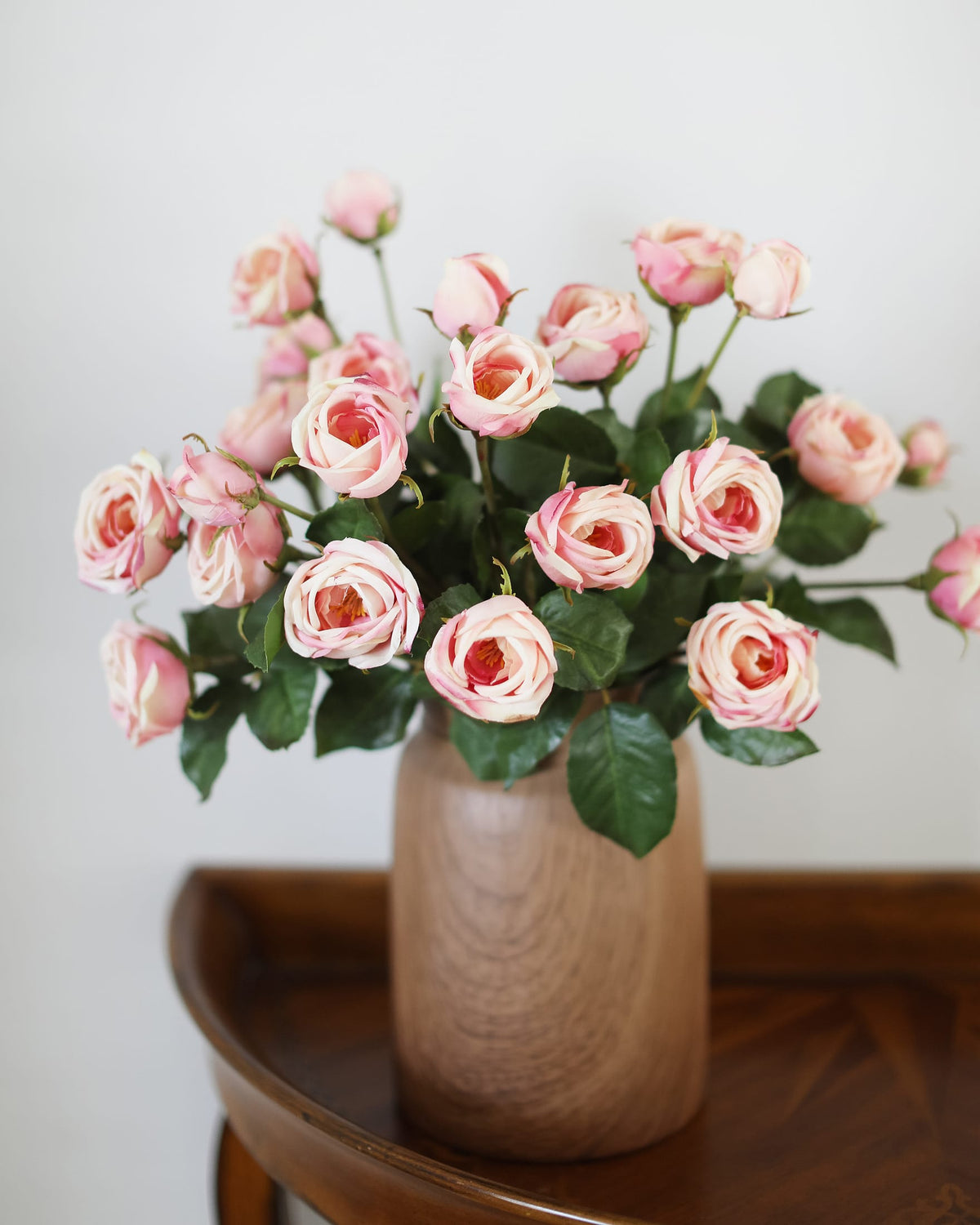 Bouquet of pink artificial roses in a wooden vase on a wooden surface with a white background
