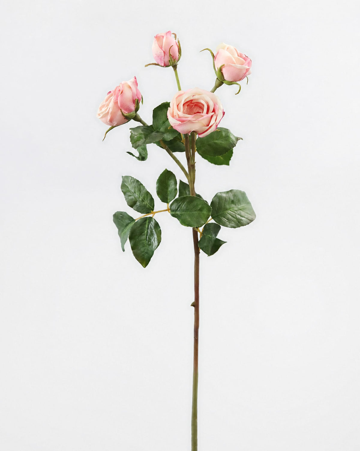 A single artificial pink rose stem with three blooms, green leaves, and a long brown stem, photographed against a plain light gray background.