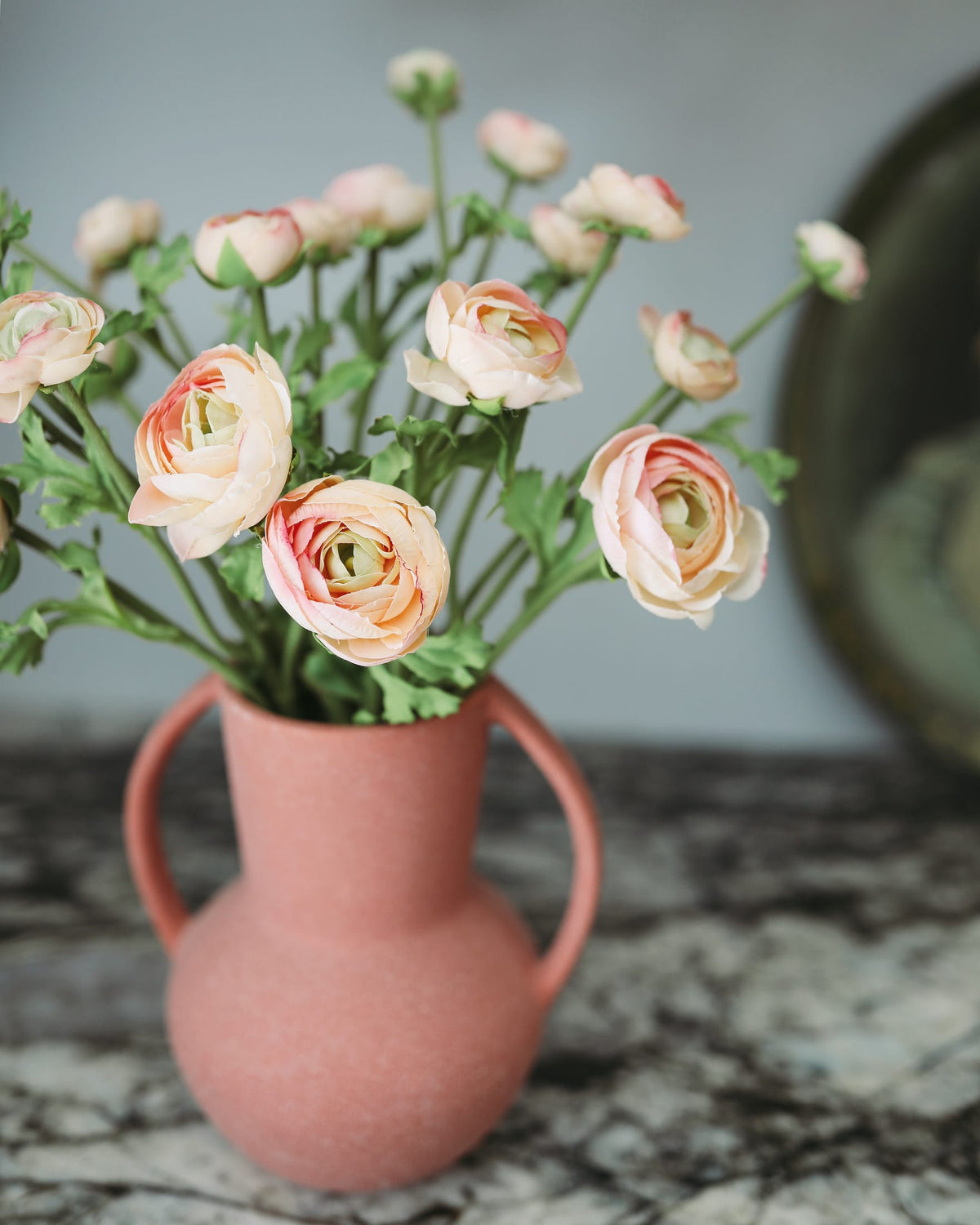 Pink vase with peach-colored faux ranunculus on a marble surface