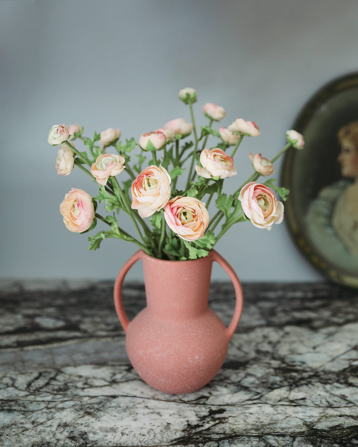 Pink vase with faux ranunculus on a marble surface