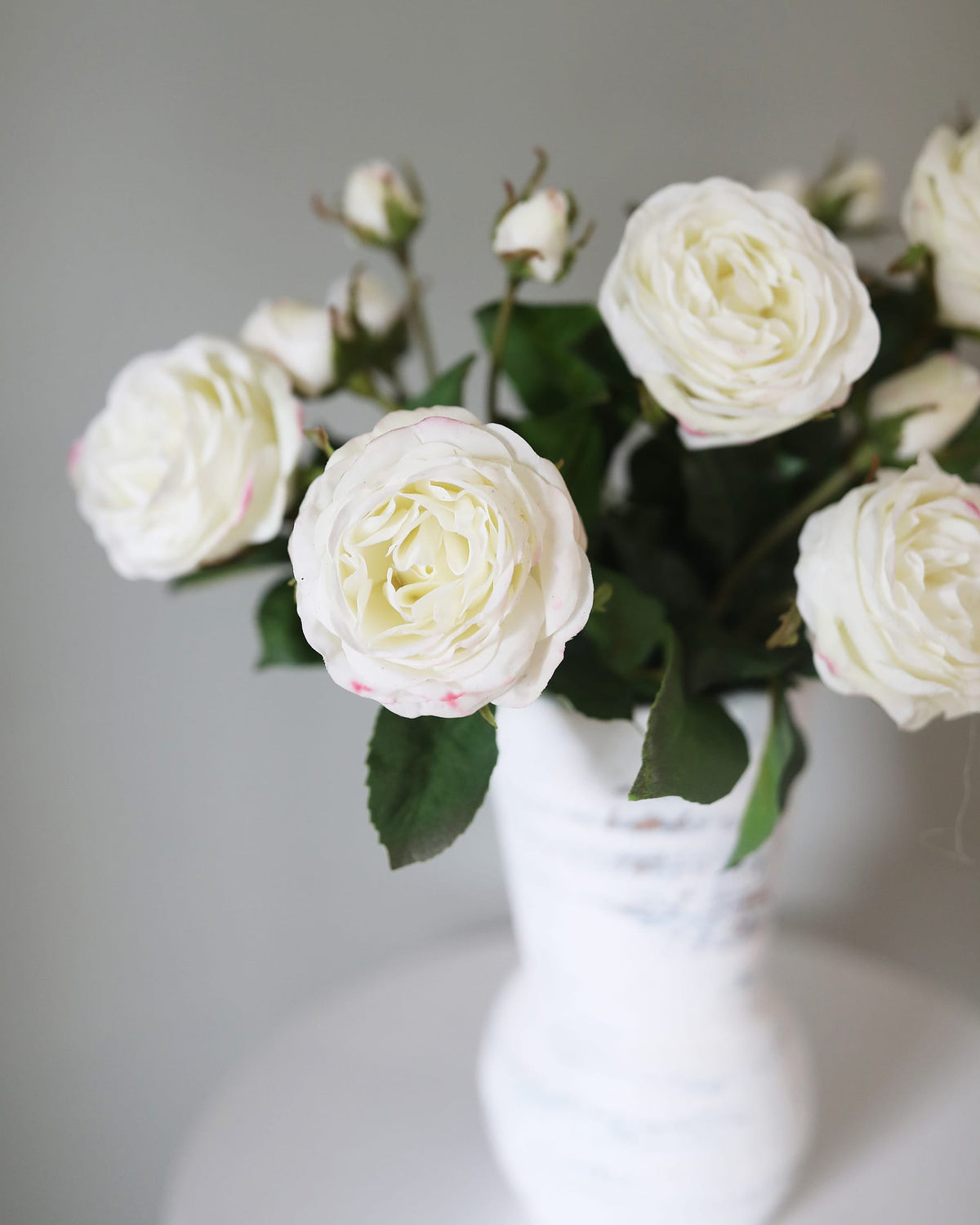 Artificial white real touch roses arranged in a white vase on a light gray background.