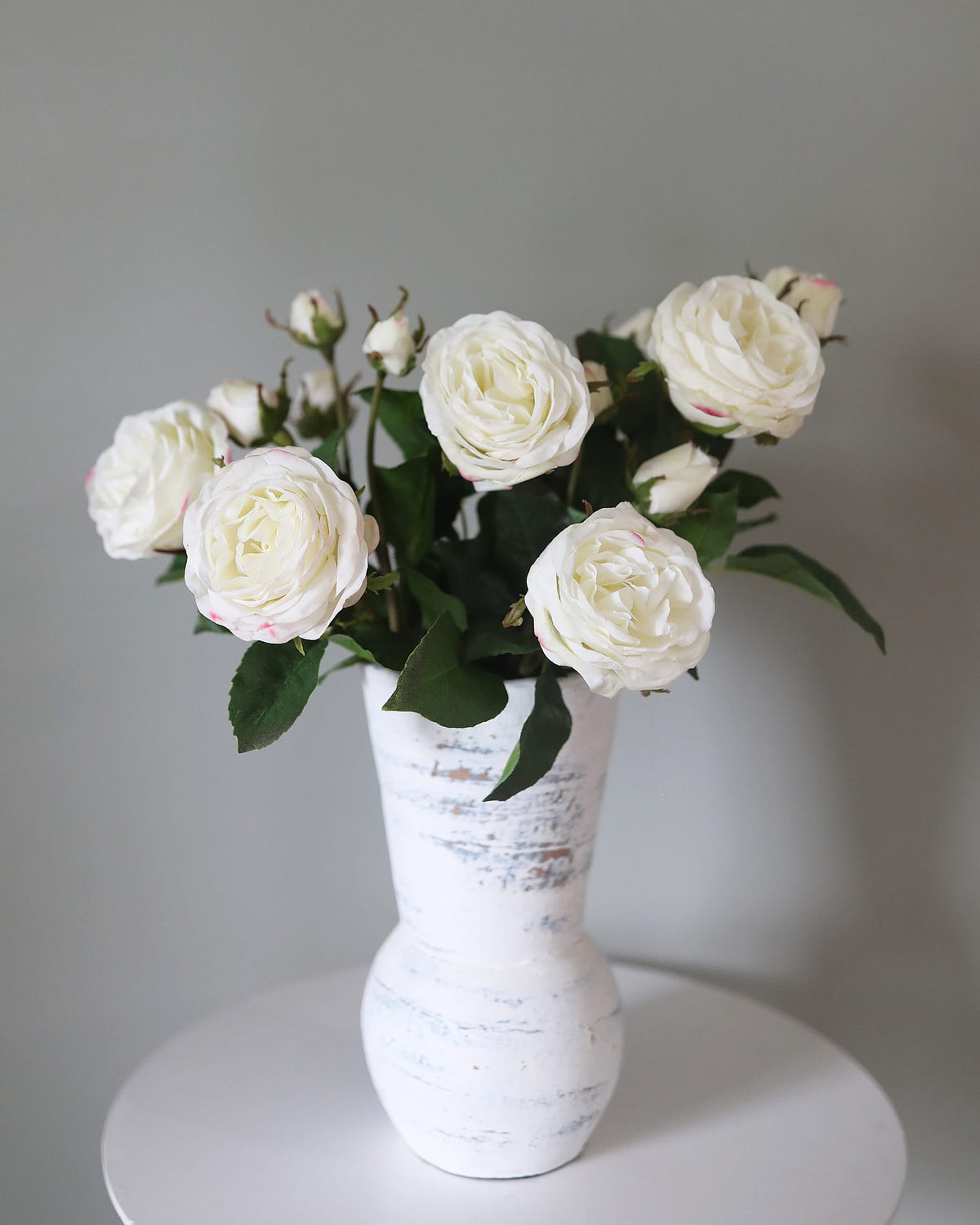 Artificial white real touch roses displayed in a white vase against a neutral background.