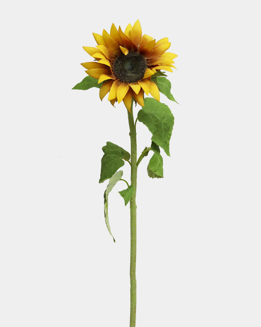 A single artificial sunflower with bright yellow petals, a dark brown center, and green leaves on a long stem, isolated on a light gray background.