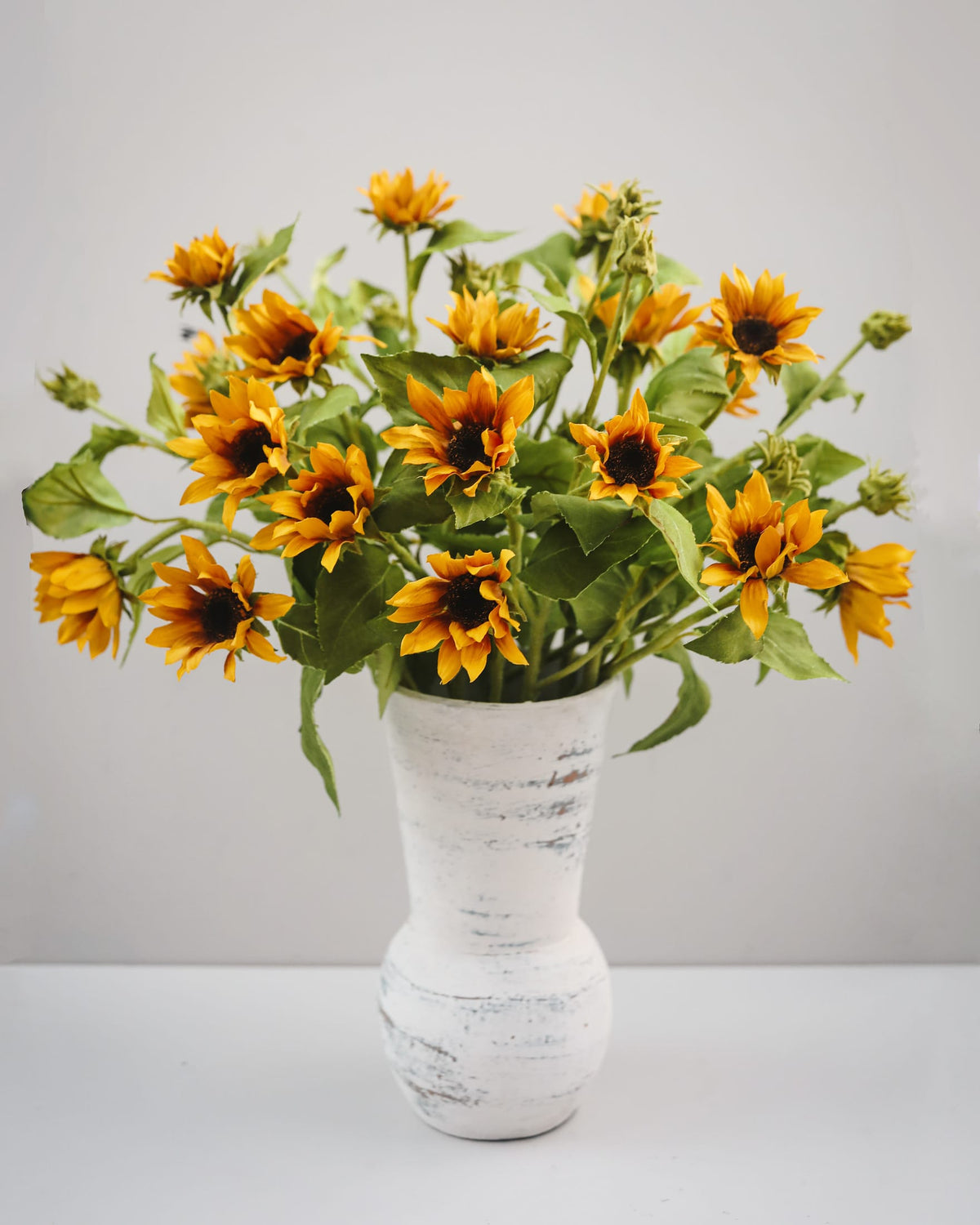 Bouquet of faux sunflowers in a white textured vase on a light background