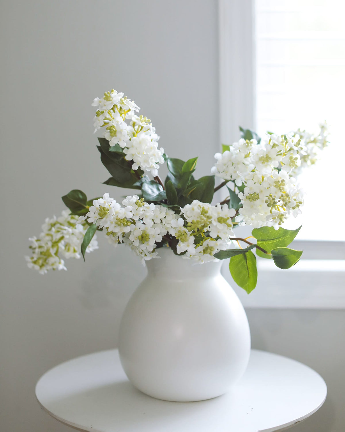 White vase with Artificial lilac on a white surface
