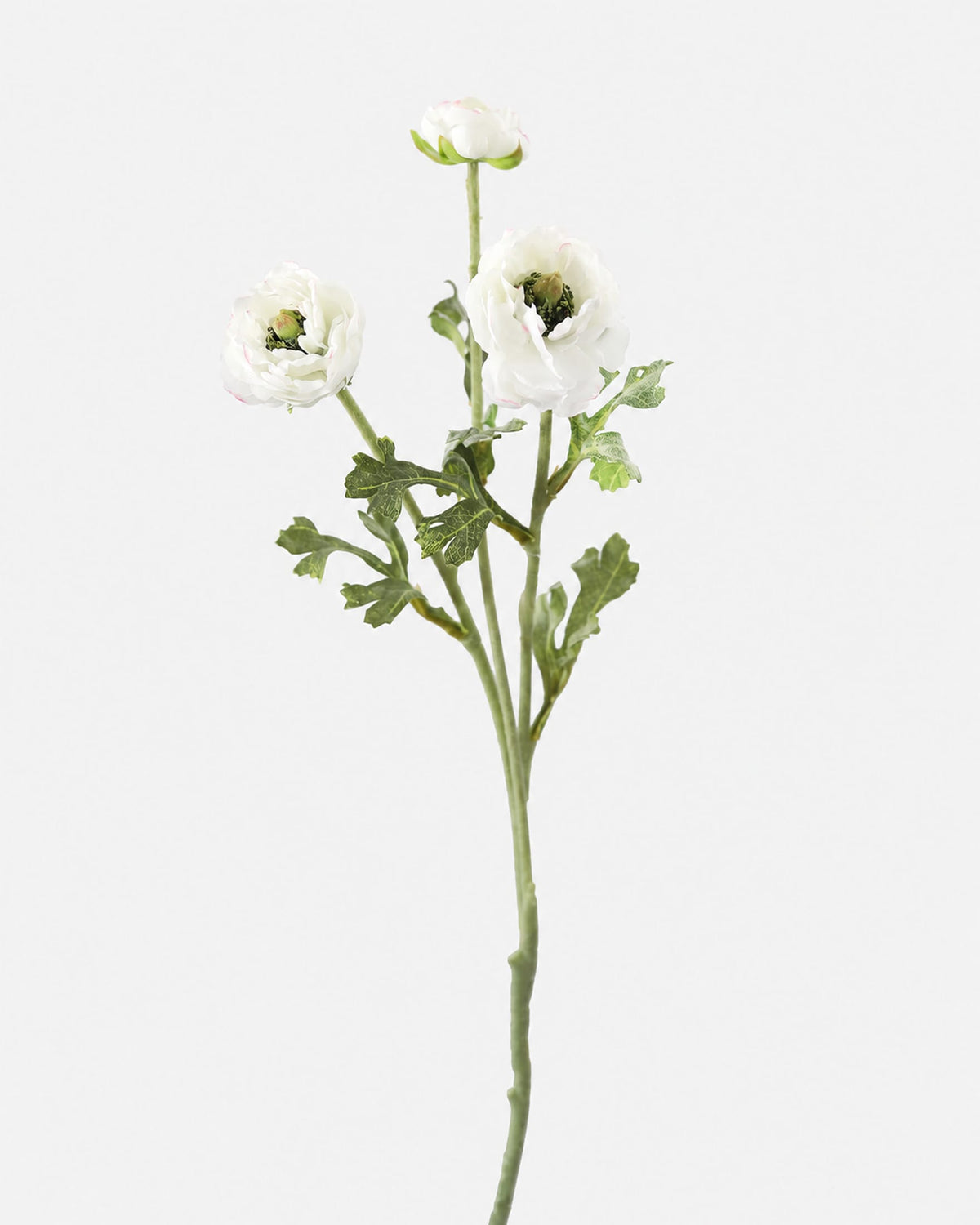 A single artificial flower stem with three white ranunculus blooms, green ruffled foliage, and a long green stem, photographed against a plain light gray background.