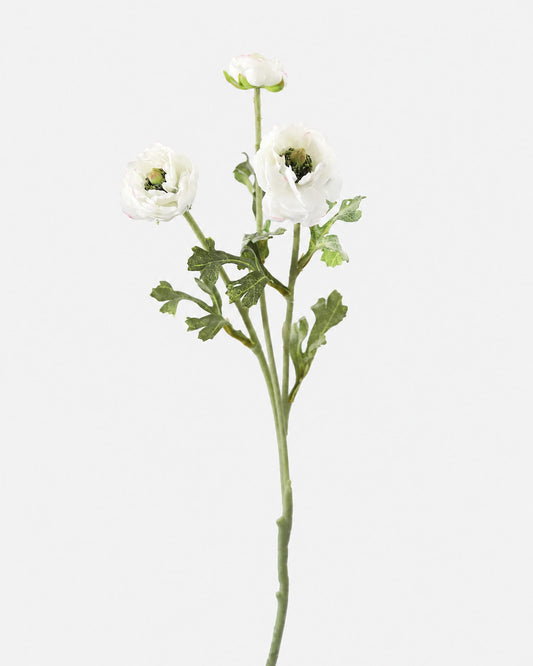A single artificial flower stem with three white ranunculus blooms, green ruffled foliage, and a long green stem, photographed against a plain light gray background.