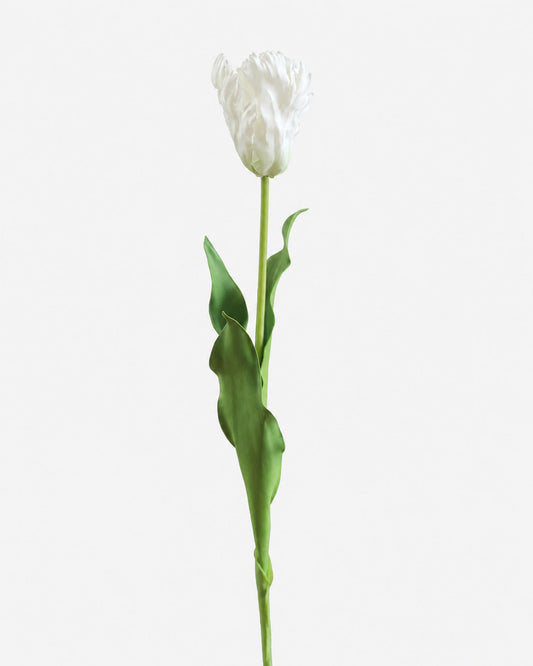 A single white faux tulip stem with a fully bloomed white flower head and green leaves, photographed against a clean light gray background.