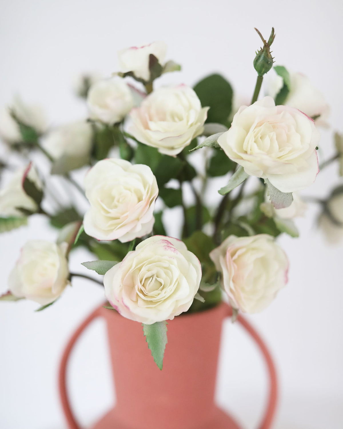 White faux roses in a pink vase on a white background