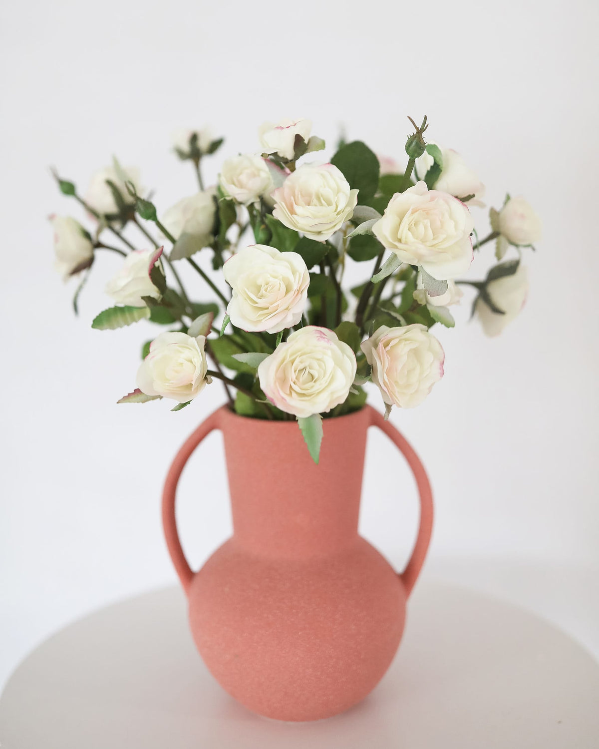 Pink vase with faux white roses on a white background