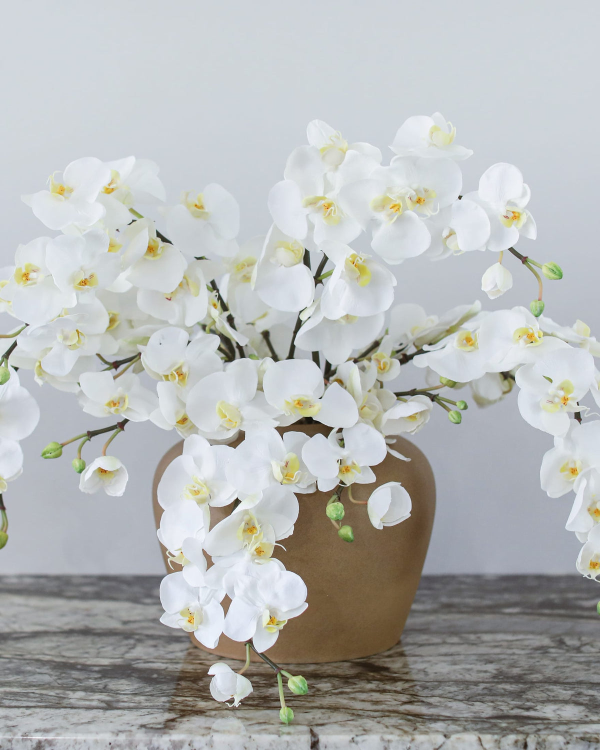 Artificial white Phalaenopsis orchids cascading from a ceramic vase for home decor.