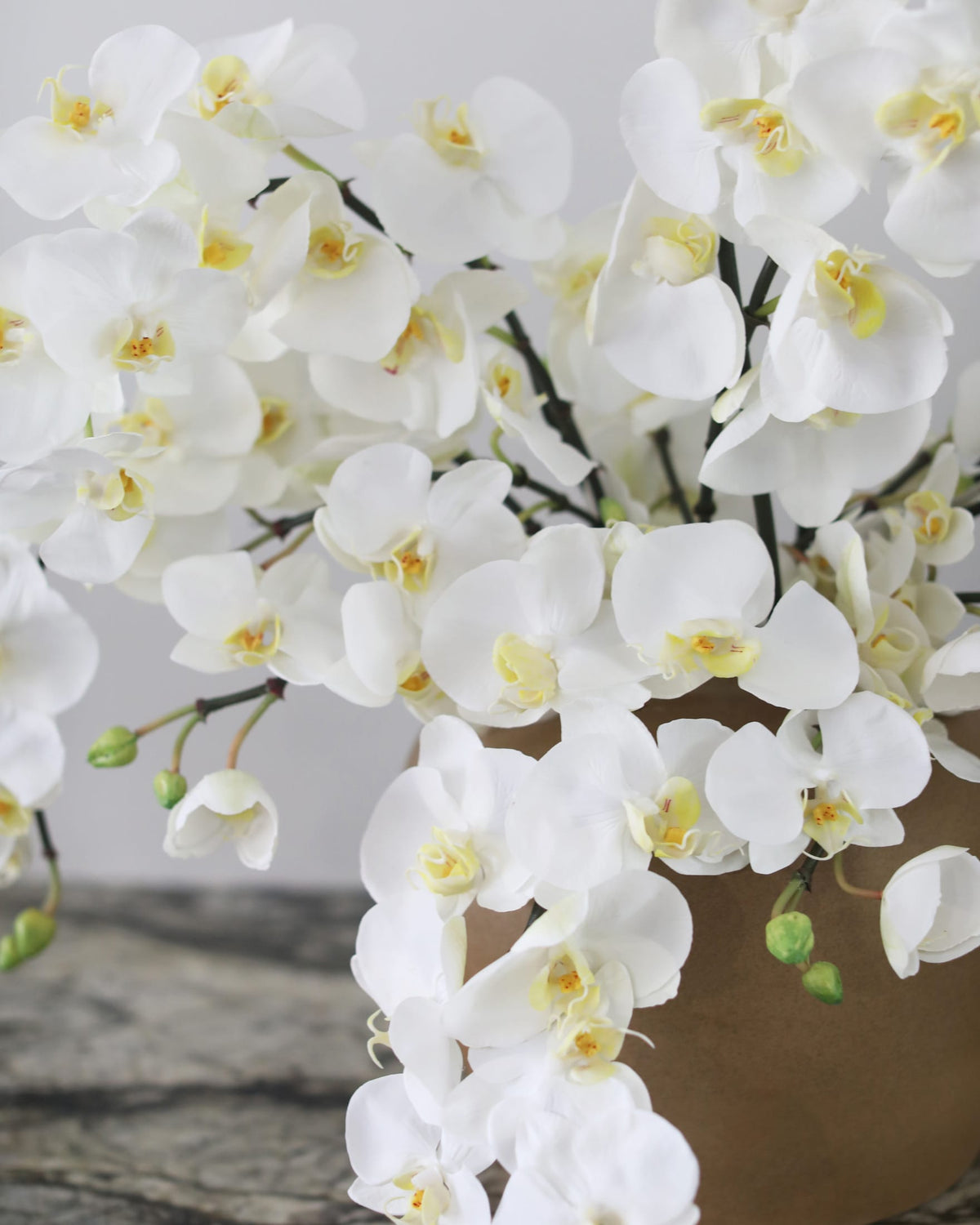White artificial Phalaenopsis orchids in a ceramic vase for elegant home styling.