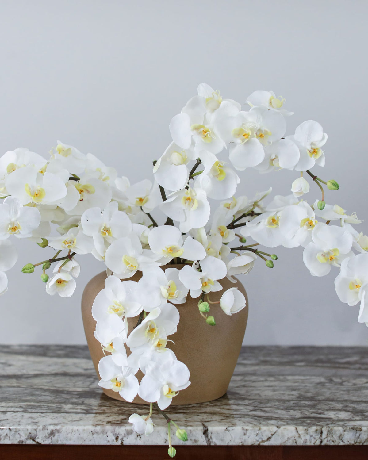 White artificial Phalaenopsis orchids arranged in a ceramic vase on a rustic table.