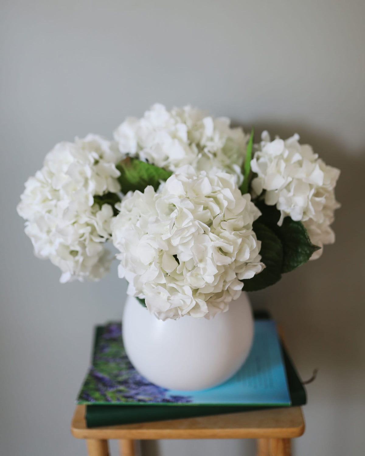 White faux hydrangea arrangement in a vase on a wooden surface with a gray background