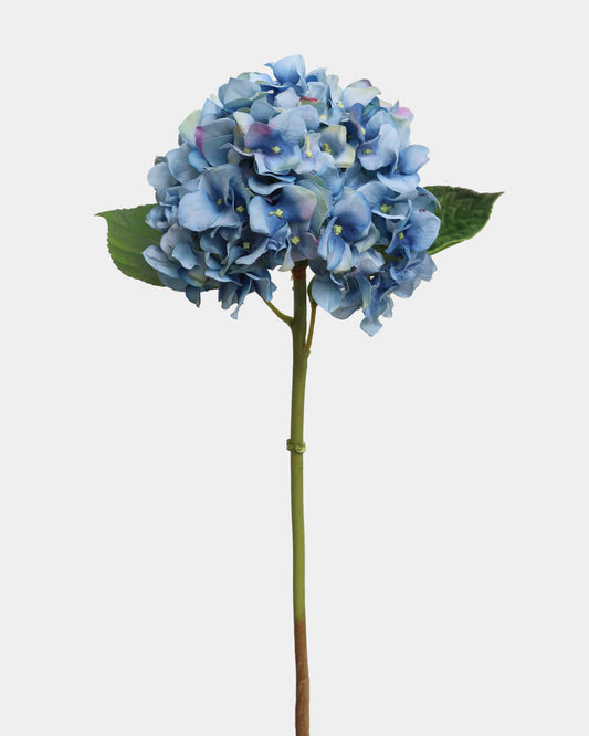 A single artificial blue hydrangea stem with green leaves, isolated on a light gray background.