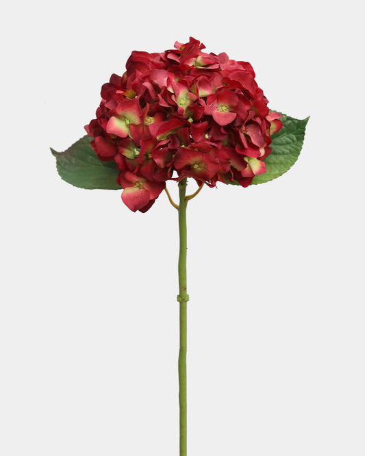 Red artificial flower with green leaves on a white background