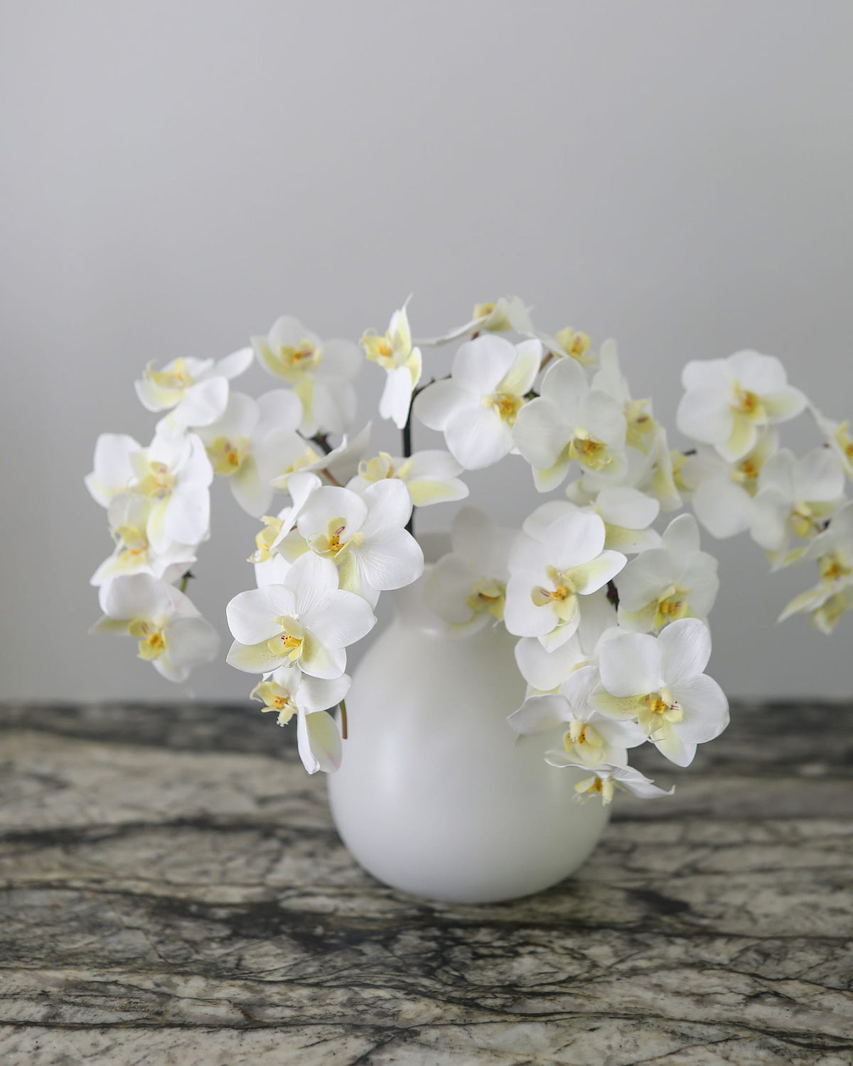 White artificial Phalaenopsis orchids arranged in a white vase for elegant home styling.