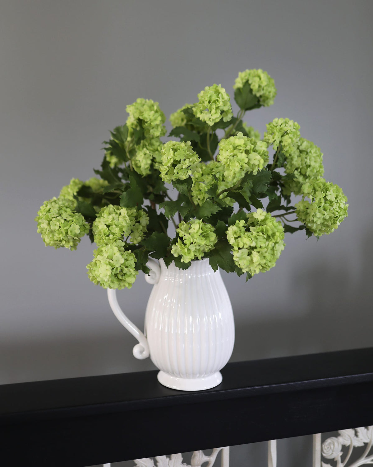 White vase with Green Faux Snowballs on a dark surface against a gray background