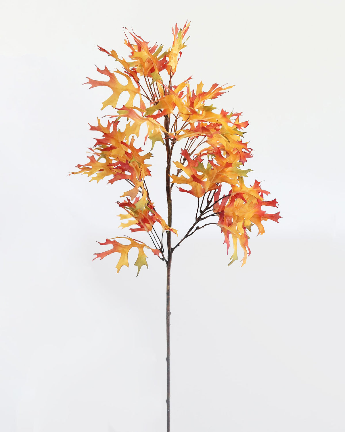 An artificial autumn leafy branch with orange, red, and yellow leaves on a brown stem, photographed against a plain white background.