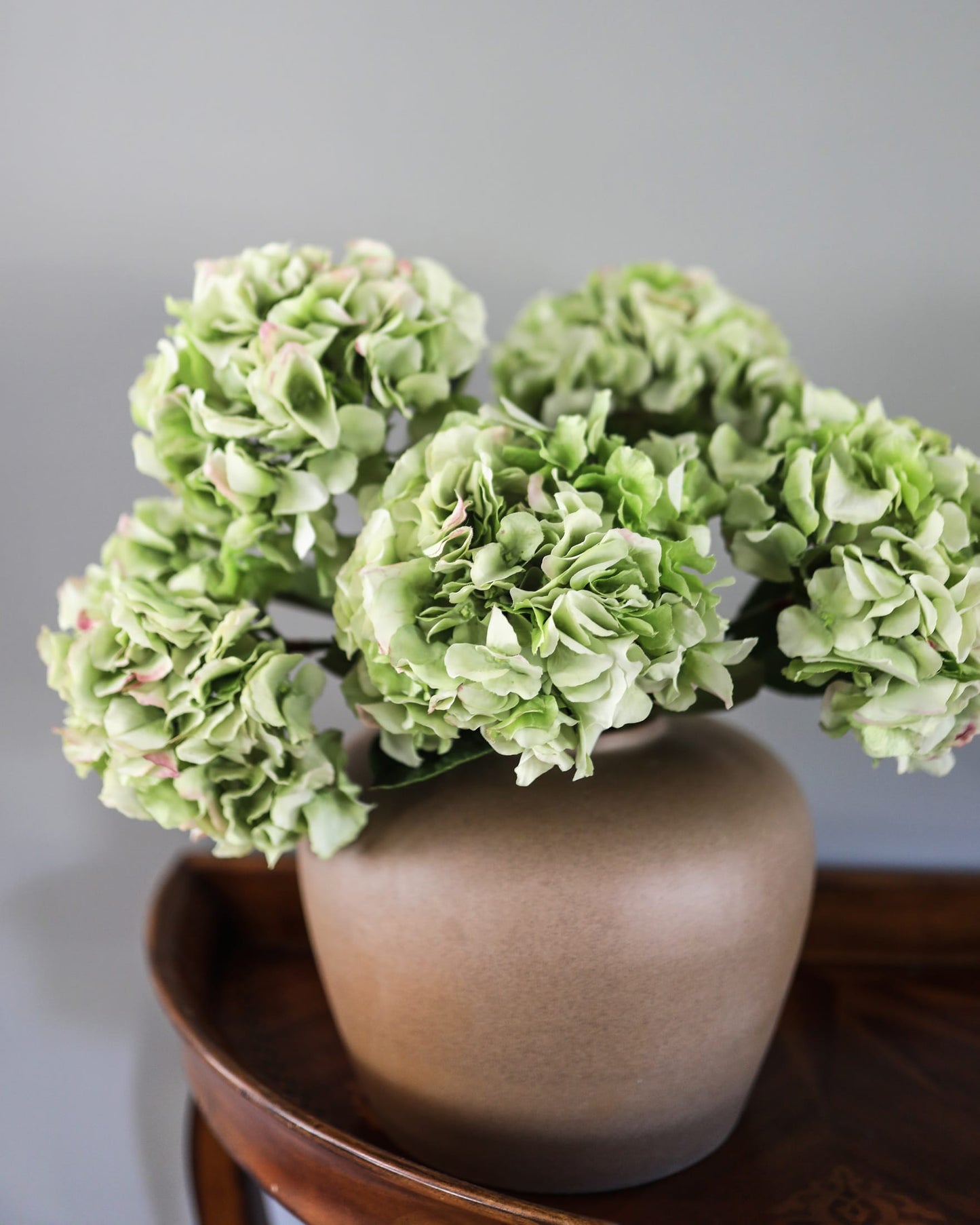Artificial green real-touch hydrangeas arranged in a matte brown vase on a dark wooden surface.