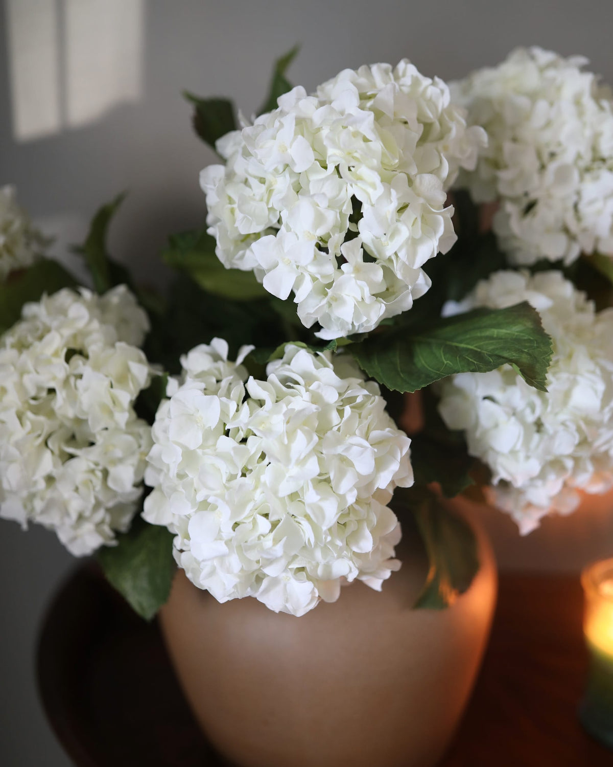 Artificial white double hydrangea flowers arranged in a vase with a softly blurred background.