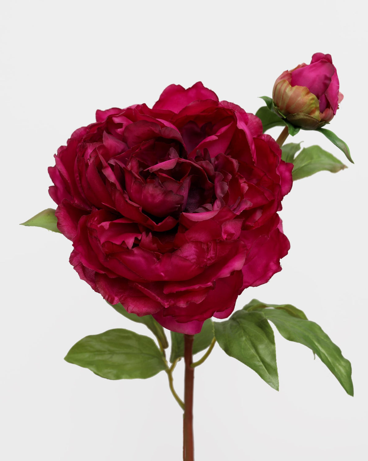 A single artificial peony stem with a large deep magenta bloom, a smaller bud, and green leaves on a plain light gray background.