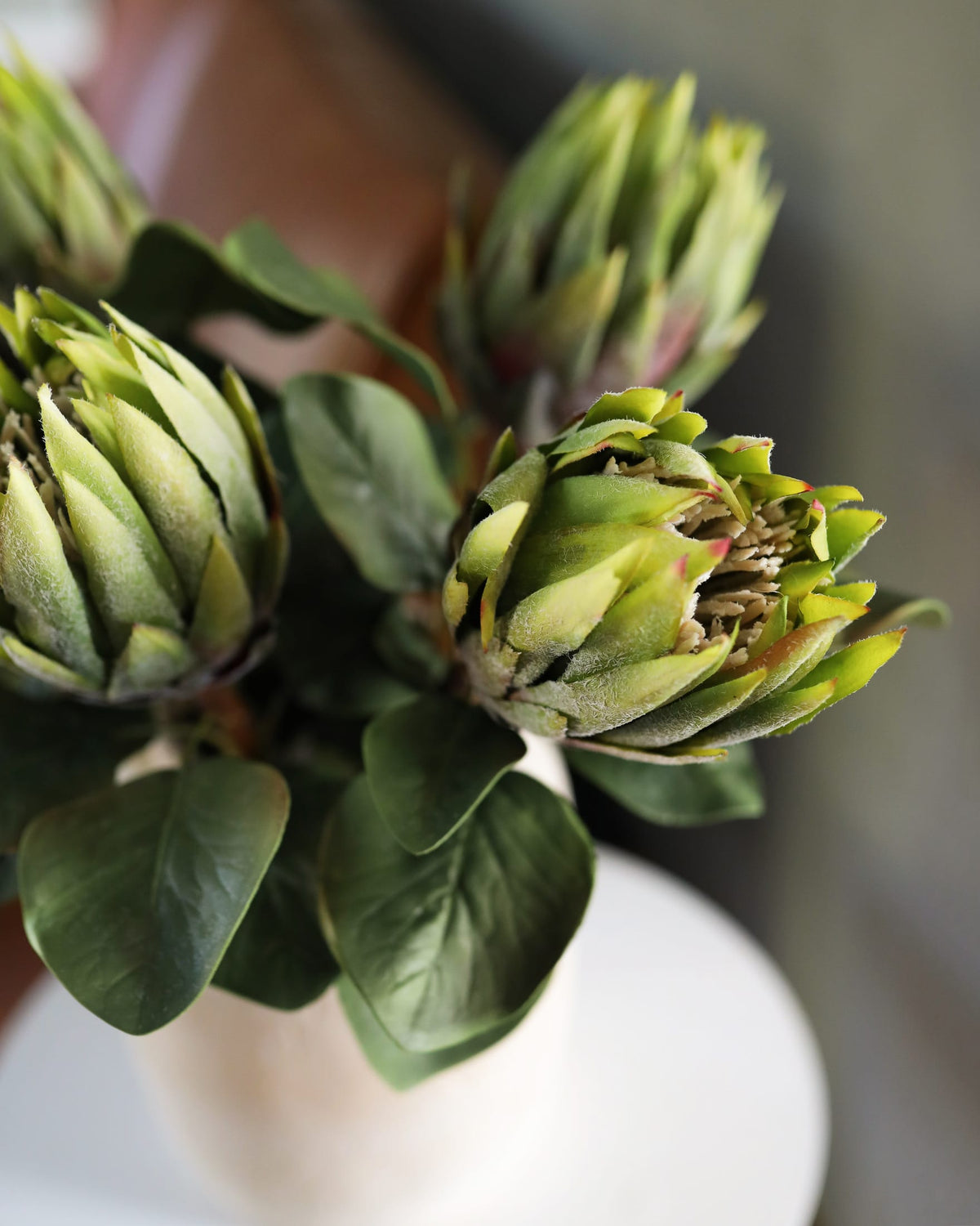 Close-up of faux green proteas on a white surface