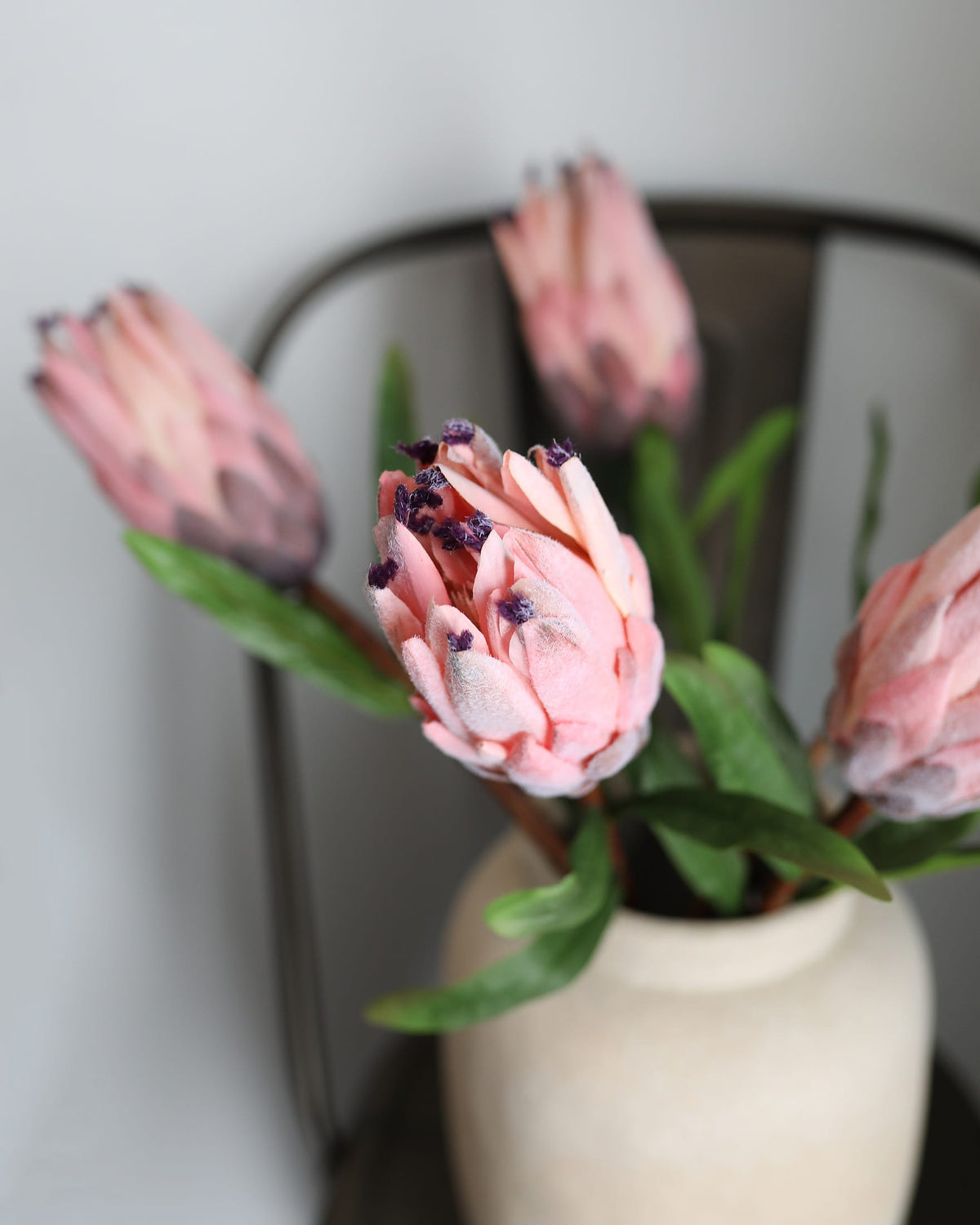 Pink faux protea flowers in a white vase against a neutral background