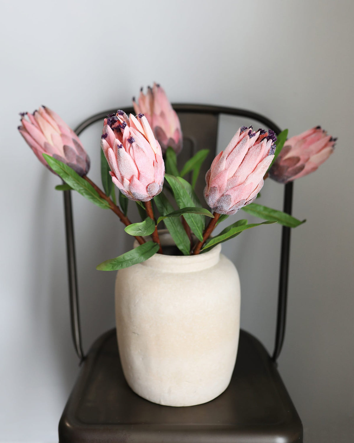 White vase with faux pink protea flowers on a dark surface against a light background