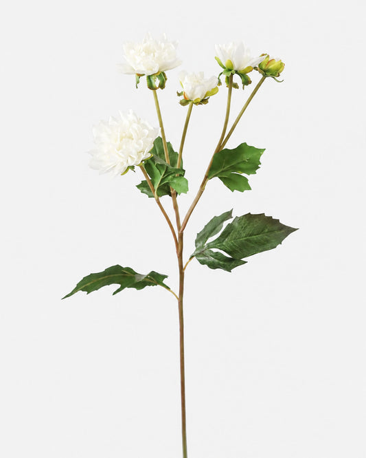 A single artificial white dahlia stem with green leaves and buds, photographed against a plain light gray background.