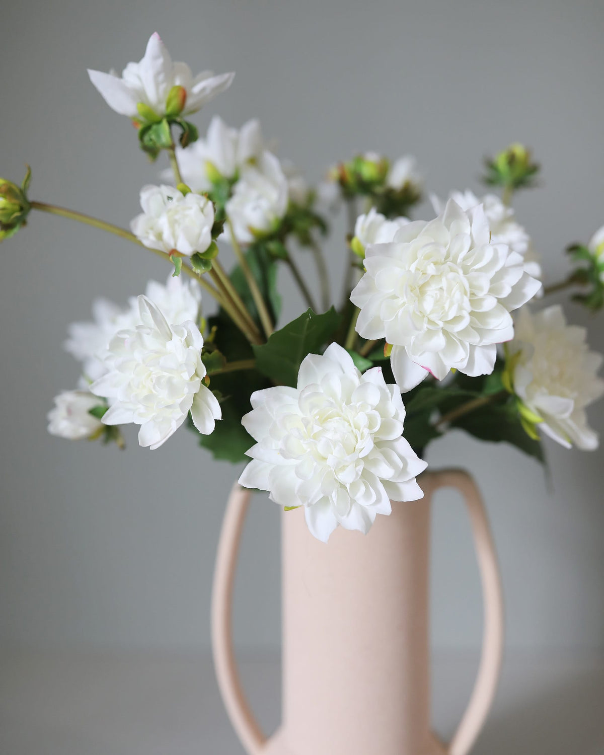 White faux dahlias in a beige vase against a gray background