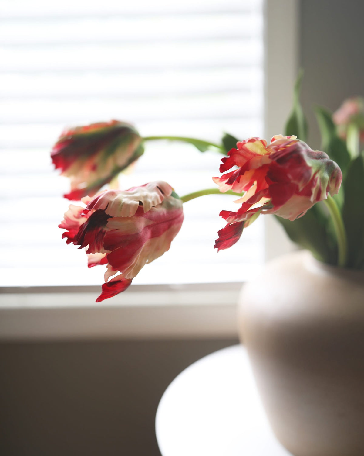 faux red tulips in a vase near a window with blinds